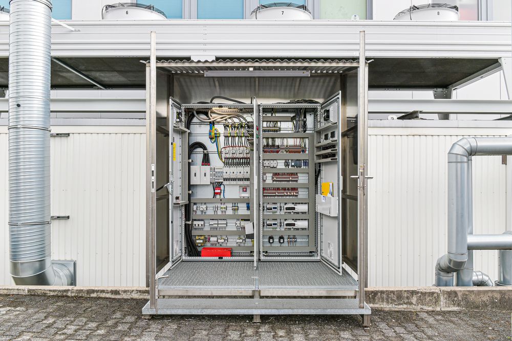 Geöffneter Schaltschrank in seiner wetterfesten Einhausung am Container, darüber die Ventilatoren des Verflüssigers